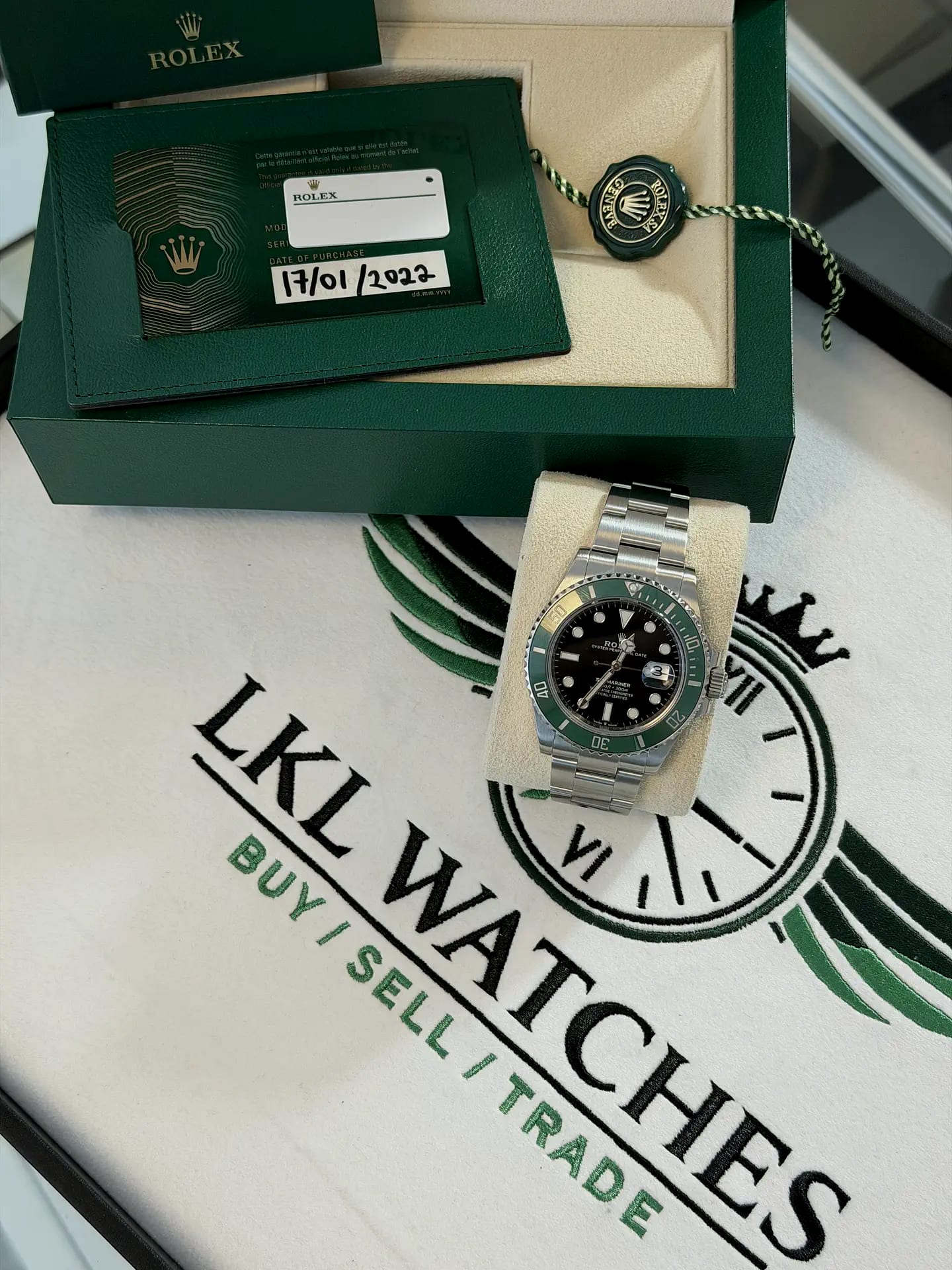A green-bezel Rolex Submariner with its green Rolex box, guarantee card and hang tag, laid out on an LKL Watches branded cloth
