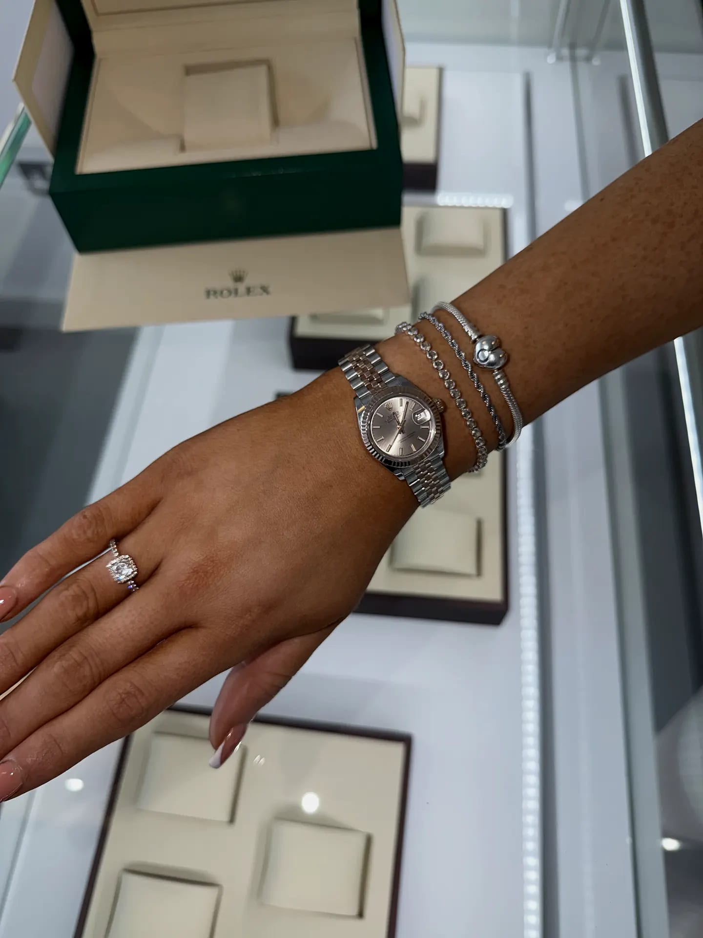 A Rolex Datejust with a fluted bezel and a pink-toned dial, worn on the wrist beside its green Rolex box in the LKL Watches showroom