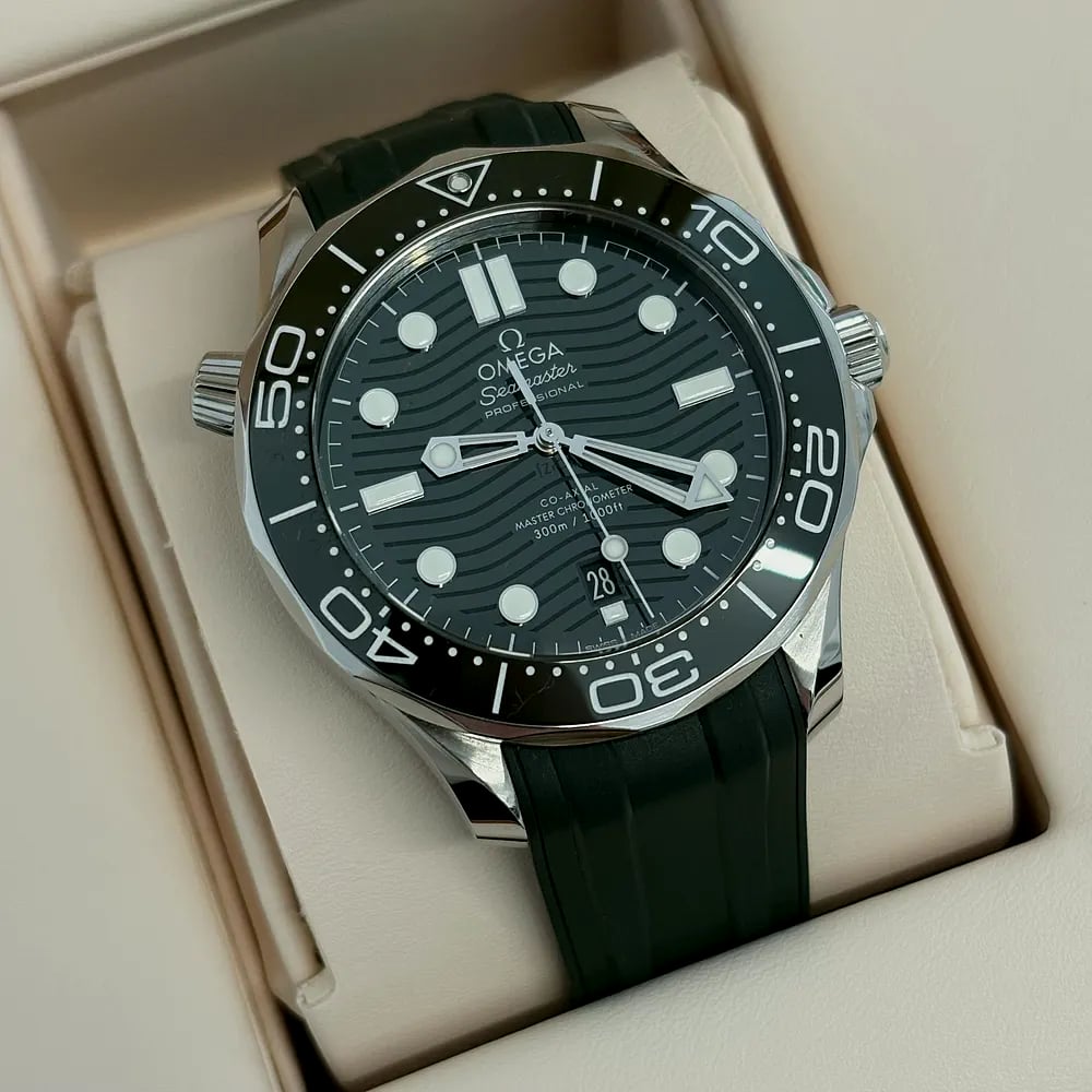 An Omega Seamaster Diver 300M with a black wave dial on a green rubber strap, in its box